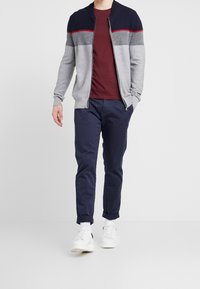 Grå zip-up cardigan med marinblå detaljer, vinröd t-shirt och mörkblå byxor. Vita sneakers med uppvikta cuffs fulländar outfiten.
