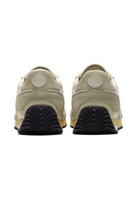 Sneakers med en överdel i krämfärgad och ljusbrun mocka, med en svart gummiyttersula som har ett texturerat mönster och cirkulära detaljer vid hälen.