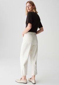 Top corto a maniche corte in maglia di colore marrone scuro, abbinato a pantaloni beige chiaro a vestibilità rilassata. Le scarpe sono di un beige chiaro con suola piatta.
