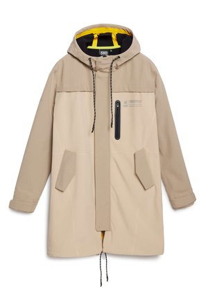 Béžová zimní bunda s kapucí, která má zipovou kapsu, šňůrky na stažení a dvě boční kapsy; uvnitř je podšívka ze žluté látky.