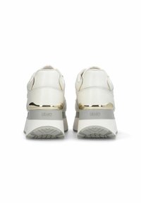 Un paio di sneakers a zeppa bianche con suole grigie e dettagli dorati, viste da dietro su uno sfondo bianco.