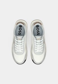 Sneaker bianche con una parte superiore in pelle liscia e dettagli grigi, dotate di una suola testurizzata e del marchio "BOSS" sulla linguetta e sul lato.