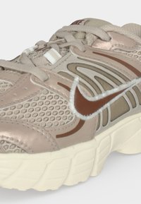 Μπεζ και καφέ αθλητικό παπούτσι Nike με διχτυωτές επιφάνειες, παχιά λευκή σόλα και κεντημένο λογότυπο Swoosh στο πλάι.