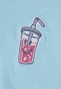 Tissu bleu bébé avec un graphique brodé d'une tasse souriante avec une paille, contenant un liquide rouge et des bulles blanches, entouré de blanc.