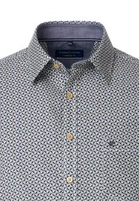 Comfort fit shirt in cream with navy leaf pattern, button-up front, and collar; features embroidered logo on small chest pocket.