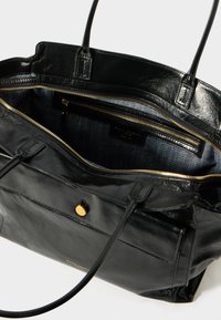 Fekete bőr tote táska sima textúrával, arany kiegészítőkkel és két hosszú fogantyúval. Belül cipzáras zsebekkel és arany színű cipzárral rendelkezik.