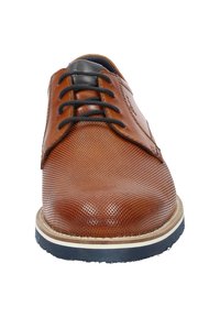 Scarpa da uomo in pelle perforata marrone con lacci neri, superficie testurizzata, punta arrotondata e accentuazione della suola in gomma bianca e blu navy.