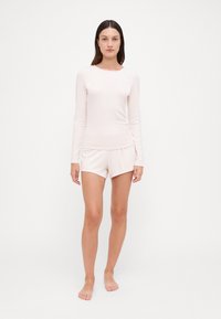 Ruosteenpunainen loungewear-asukokonaisuus, jossa on pitkähihaista toppia pyöreällä kaula-aukolla ja vastaavat sortset joustavalla vyötäröllä. Pehmeä, viistopintainen rakenne.