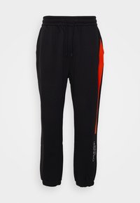 Black sweatpants with an orange stripe along the side, elastic waistband with drawstring, and tapered cuffs. Features logo detail near hem.