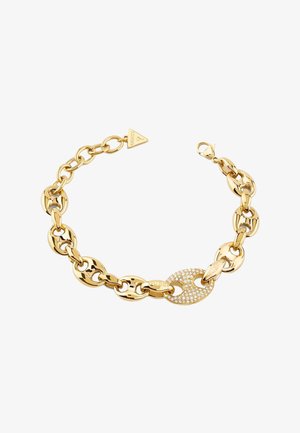 Armband met gouden schakels, bestaande uit grote ovale schakels, een sprankelende met kristallen bezette schakel en een driehoekige merkbedel, op een witte achtergrond.