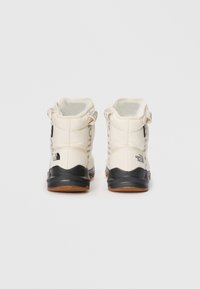 White insulated boots with a textured black rubber sole, featuring a padded collar, adjustable straps, and side branding.