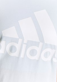 Camiseta de algodón azul claro con un gran logo blanco de Adidas, de textura suave y un efecto degradado que va de un azul claro a uno más oscuro.