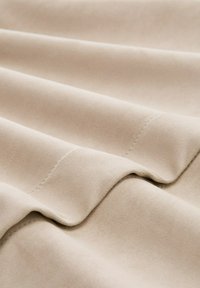 Tela beige con una textura suave, que presenta suaves caídas y sutiles detalles de costura, dispuestas en suaves olas.