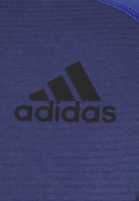 Tessuto atletico viola con un logo Adidas nero. La texture è liscia con un motivo a maglia e c'è una leggera lucentezza in alcune condizioni di illuminazione.