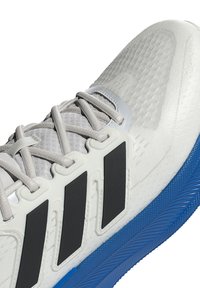 Weißer und grauer Sportschuh mit schwarzen Streifen, grauen Schnürsenkeln, strukturiertem Zehenbereich und blauer Sohle.