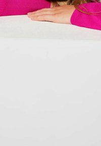 Pull fuchsia à texture côtel ée, couvrant partiellement une surface blanche. Mains reposant sur la surface, doigts détendus.