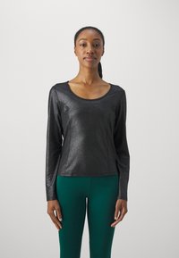 Svart langermet topp i et skinnende materiale med rund hals, med tilpassede sider og en glatt tekstur, satt sammen med grønne leggings.