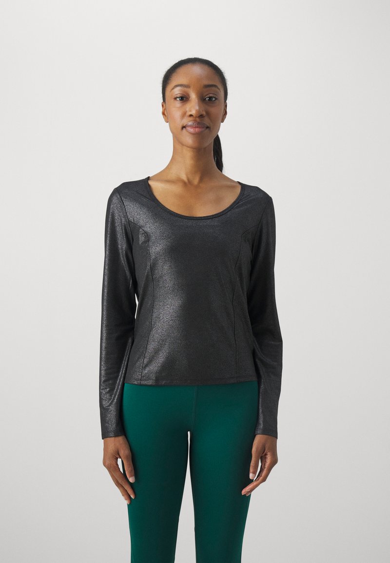 Svart langermet topp i et skinnende materiale med rund hals, med tilpassede sider og en glatt tekstur, satt sammen med grønne leggings.