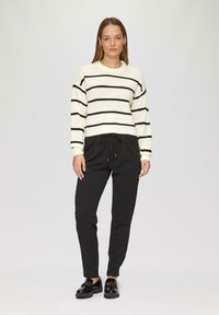 Gestreepte gebreide trui in crème met zwarte strepen, gecombineerd met zwarte joggerpants en zwarte gepatenteerde schoenen. Eenvoudig, casual ontwerp.
