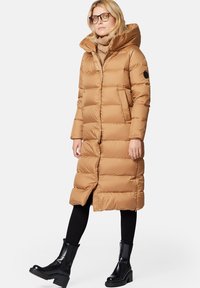 Długi puchowy płaszcz w kolorze tan z wysokim kołnierzem i zapięciem na zamek. Posiada poziome przeszycia, kieszenie boczne oraz czarną naszywkę z logo na rękawie.
