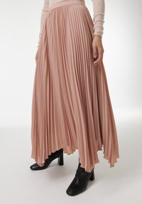 Geplooide midi-jurk in een zachte roze stof, met een hoge tailleband en een vloeiende uitstraling, gecombineerd met zwarte hoge enkellaarsjes.