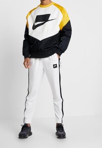 Svart och gul Nike-tröja med en stor logotyp, tillsammans med vita byxor med svarta sidränder och en liten logotyp-patch.