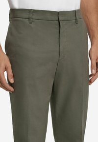 Olivgrüne Hosen mit einem strukturierten Fischgrätmuster, flacher Vorderseite, seitlichen Taschen und normalem Bund.