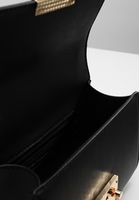 Borsa a mano in pelle nera con un design strutturato, dotata di una chiusura metallica dorata e scomparti interni per carte. Texture liscia e interno minimal.