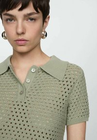Polo shirt a maglia di colore verde chiaro con motivo a nido d'ape, dotato di colletto e tre bottoni al colletto, maniche corte e tessuto testurizzato.