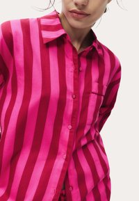 Koszula z długim rękawem i kołnierzykiem, w pionowe różowe i czerwone paski, z kieszonką na piersi i zapięciem na guziki, uszyta z gładkiego materiału.