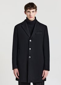 Schwarzer Wollmantel mit Reverskragen, fünf Knöpfen zum Schließen, Seitentaschen und schlanker Passform. Getragen über einem strukturierten schwarzen Rollkragenpullover.