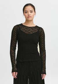 Top in pizzo nero a maniche lunghe con scollatura rotonda, motivo floreale a rilievo e silhouette aderente, abbinato a una gonna nera a balze.