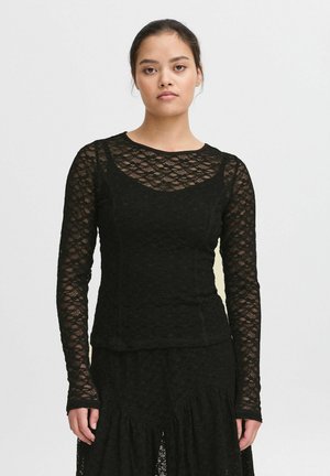 Schwarzes Langarm-Spitzenoberteil mit rundem Ausschnitt, strukturiertem Blumenmuster und figurbetonter Silhouette, kombiniert mit einem schwarzen Rüschensrock.