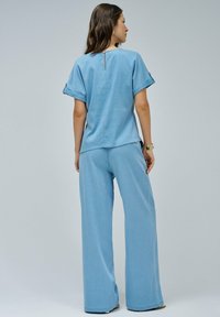 Camicia in denim azzurro chiaro abbinata a pantaloni a gamba larga dello stesso colore. La camicia presenta una scollatura a chiave, maniche corte e una vestibilità comoda.