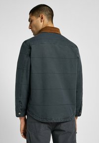 Herrejakke i mørkegrå farve med kordfløjlskrage, skrå syninger og knapmanchetter. Materialet virker glat med et afslappet design.