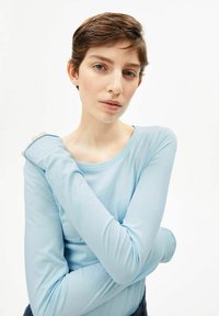 Hellblaues Langarmoberteil aus weichem Stoff mit rundem Ausschnitt. Die Ärmel sind leicht tailliert und der Stoff hat eine glatte Textur.