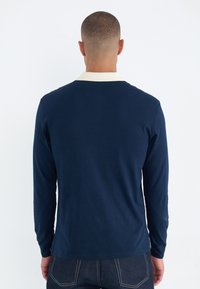 Marineblaues Langarmshirt mit einem cremfarbenen Kragen, aus weichem Stoff gefertigt. Hat ein schlichtes Design und einen geraden Schnitt mit seitlichen Schlitzen.