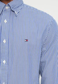 Gestreifte Button-up-Bluse in Blau und Weiß, aus Baumwolle gefertigt. Verfügt über einen klassischen Kragen und ein kleines, gesticktes Logo in Rot und Schwarz.