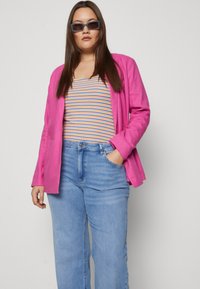 Bright pink blazer over a striped tank top featuring orange, blue, and yellow. Light blue wide-leg jeans with front pockets.