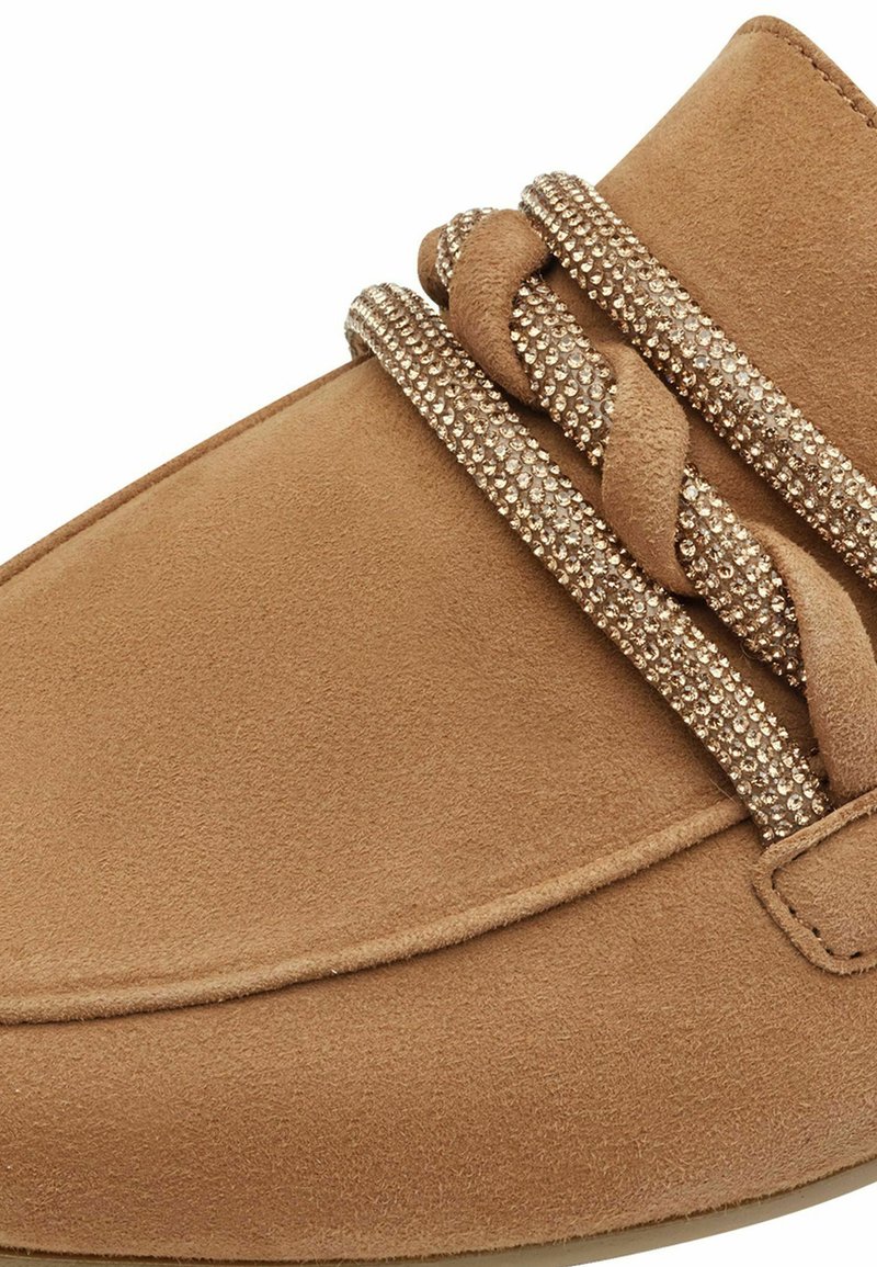 Chaussure en suède beige avec un design tressé et des embellissements scintillants. Texture lisse avec un bout rond et des coutures décoratives.