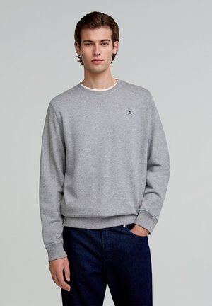Grijze sweatshirt van katoen met een ronde hals, ribgebreide manchetten en onderzoom. Heeft een klein geborduurd logo op de borst. Gemaakt in combinatie met donkerblauwe jeans.