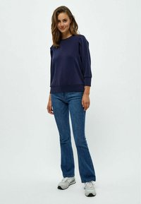 Sudadera de color azul marino con mangas 3/4, puños acanalados y un corte relajado, combinada con jeans de mezclilla acampanados y zapatillas blancas.