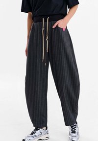 Pantaloni largi, gri închis, cu dungi subțiri deschise, talie elastică, șnururi contrastante și buzunare laterale. Asortați cu adidași argintii.