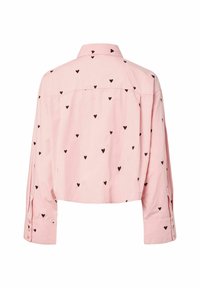 Chemise courte rose avec un col à boutons, ornée de motifs en forme de cœurs noirs dispersés. Manches longues avec des détails à boutons aux poignets.