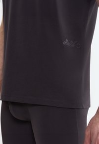 Top sportivo a maniche corte in tessuto grigio scuro, caratterizzato da un design minimalista con un logo discreto vicino all'orlo e una texture liscia.