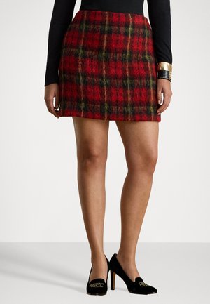 Piros és fekete kockás mini szoknya texturált anyagból, fekete, arany kiegészítővel rendelkező sarkú cipővel párosítva. A szoknya testhez simuló fazonú.