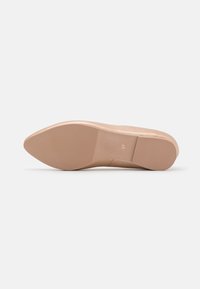 Chaussure nude à bout pointu avec un dessus synthétique lisse, un talon fin et une semelle en caoutchouc texturée présentant des lignes horizontales pour une meilleure adhérence.