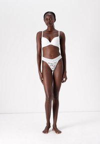 White padded bra with adjustable straps and lace trim; matching white lace thong with a v-shaped waistband and intricate lace pattern.