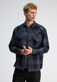 Zwart en marineblauwe geruite flanellen shirt met drukknoopsluiting, twee borstzakken en een klassieke kraag. Draag het over een grijze T-shirt met een ontspannen pasvorm.
