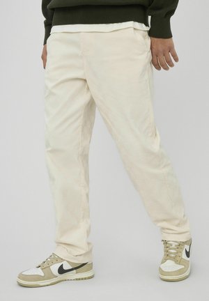 Pantalon en velours côtelé beige clair avec une texture côtelée verticale, associé à des baskets Nike beige et blanches avec des accents noirs.